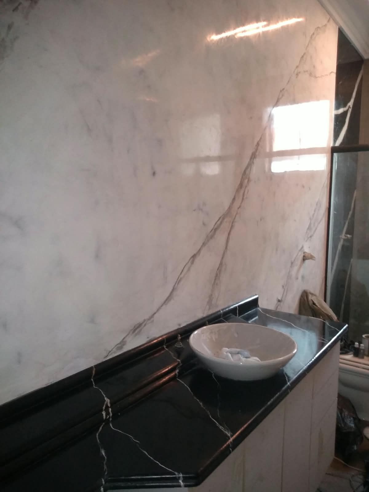 Banheiro com parede em marmorato branco e bancada preta com cuba de apoio