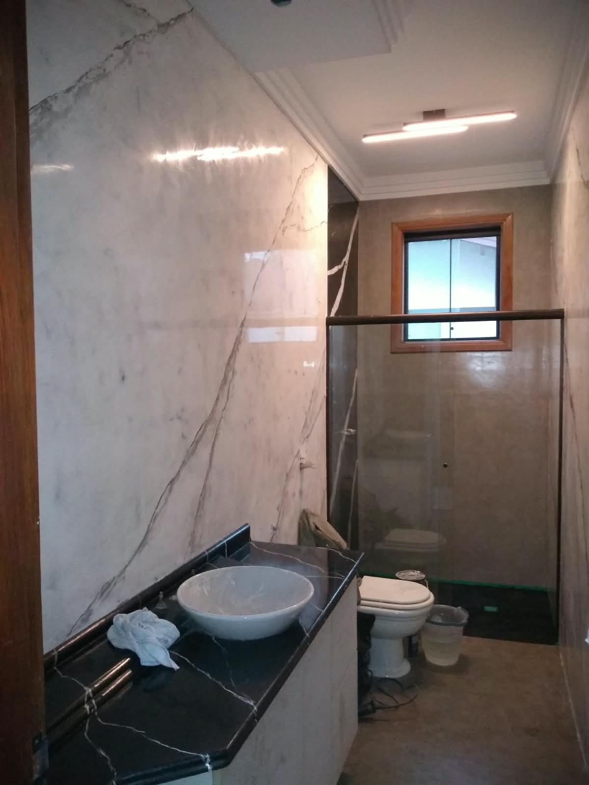 Banheiro com paredes em marmorato branco veiado e bancada preta, obra do Shamir Marmorato